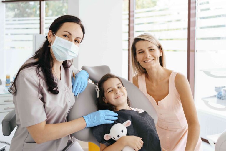 Smiling child patient with dentist and parent in a dental office.
