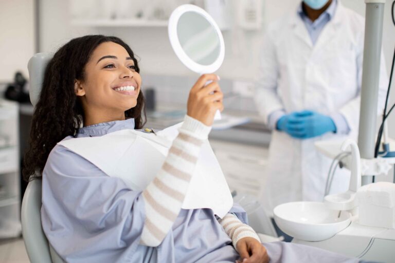 Patient smiling while checking teeth in a mirror.